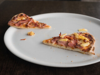 Two slices of ham and pineapple pizza on large white plate on table with natural light