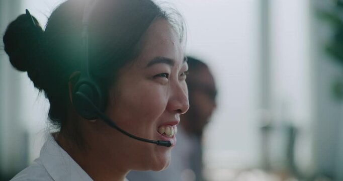 Call center office: Close up of friendly Asian technical customer support specialist in headset having conversation on call, solving problem, helping online. Female client experience officer working.