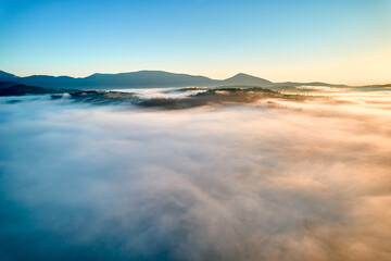 Stunning aerial view of sunrise over mountainous landscape, with thick fog blanketing valleys and...