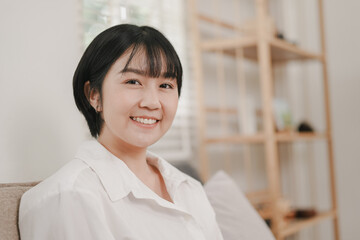 Obraz premium Smiling woman poses comfortably in modern living space, showcasing natural joy and relaxation amidst minimalist decor
