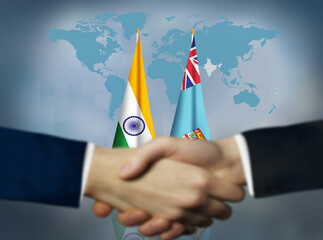 Two people shaking hands in front of Fiji and India flags