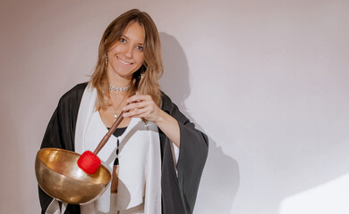Woman is doing a massage with Tibetan singing bowls in a spa salon against the beige backdrop....
