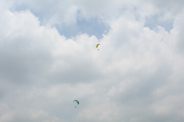 Two parachutes of paragliders with cloudy sky background