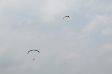 Two parachutes of paragliders with cloudy sky background