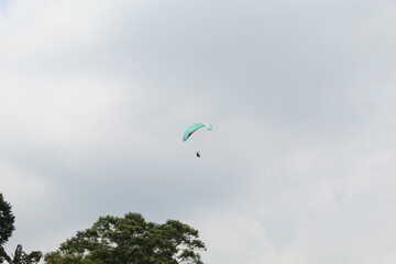 One parachute of paragliding on cloudy sky background and green trees