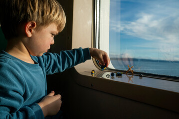 A 4 year-old boy plays with on the ledge of a ferry boat window.