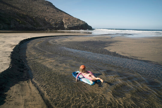 A 5 year-old girl floats on a boogie board down a shallow beach creek