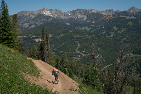 A mountain biker rides down a single-track trail with big mountains