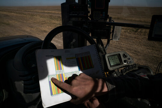 A man's hand points at the map of row crops from inside a tractor.