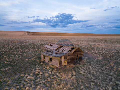 A dilapidated homesteader cabin amidst a vast prairie at sunset.