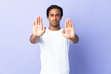 Young African American man with braids man isolated on purple background making stop gesture and...