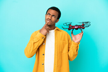African American handsome man holding a drone over isolated blue background having doubts while...