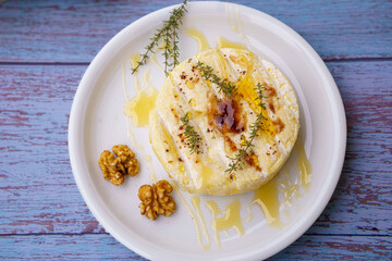 Baked Camembert, traditional creamy gourmet round cheese from France with honey, fig jam, thyme and walnuts. White plate on rustic wooden background. Close up