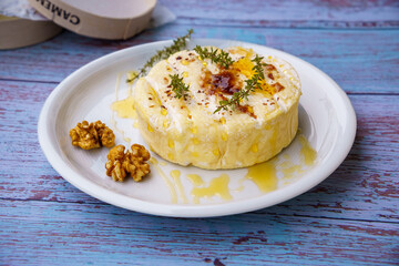 Baked Camembert, traditional creamy gourmet round cheese from France with honey, fig jam, thyme and walnuts. White plate on rustic wooden background. Close up