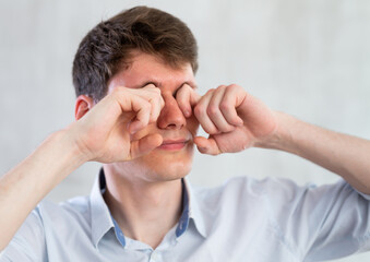 Man scretching itchy eyes on gray background
