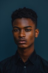 Obraz premium A close-up portrait of a young man with sharp features on a dark monotone blue background. intense lighting enhances his confident expression, creating a bold and striking visual impact