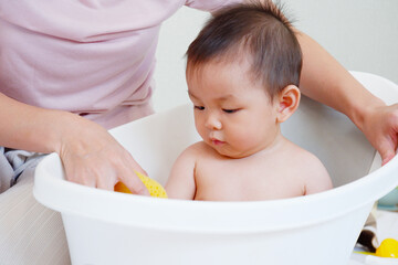 Mother is bathing her baby in a bathtub.