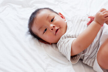 Cute little baby smiling and lying on a white bed.