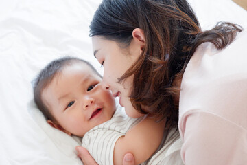 A mother and her cute little baby are lying on a white bed.
