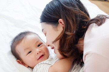 A mother and her cute little baby are lying on a white bed.
