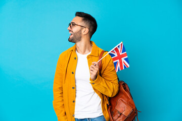 Young caucasian man holding an United Kingdom flag isolated on yellow background laughing in...