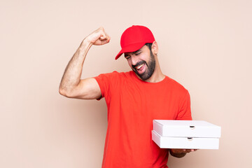 Young man holding a pizza over isolated background celebrating a victory