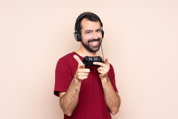 Fototapeta premium Man playing with a video game controller over isolated wall pointing to the front and smiling