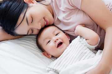 A mother and her cute little baby are lying on a white bed.