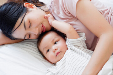 A mother and her cute little baby are lying on a white bed.