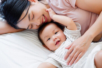 A mother and her cute little baby are lying on a white bed.