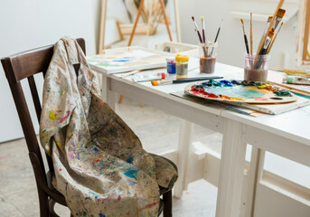 An artist's workspace with paint-stained materials and a chair ready for creative work in a bright studio