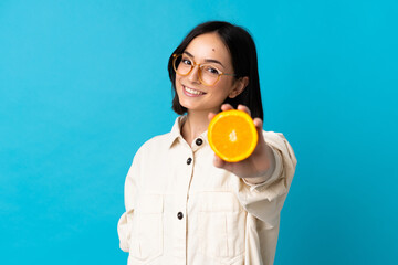 Young caucasian woman isolated on blue background holding an orange