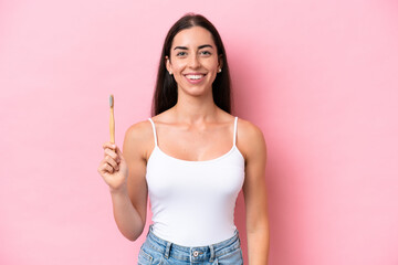 Young caucasian woman brushing teeth isolated on pink background smiling a lot