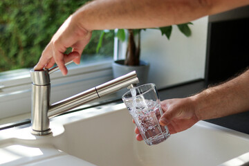 Close up of male hands pouring tap water into a glass in the kitchen