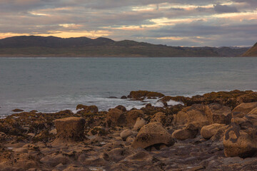 Waves crashing into coastal rocks at sunset. Dramatic sea coast background. Raglan, New Zealand