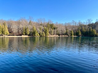 Beautiful treelined lake on a sunny winter’s day.  Bright blue sky, no people.  Water reflection of trees on the lake.  Green Lakes, Syracuse New York