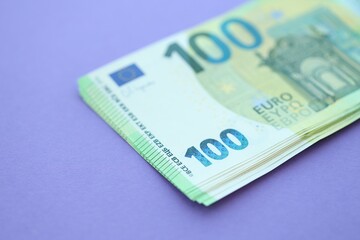 Big amount of one hundred euro money bills on lilac background