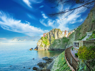 Train track is passing by a colorful Italian village overlooking the ligurian sea on a beautiful sunny day with blue skies and white clouds, in Cinque Terre National park