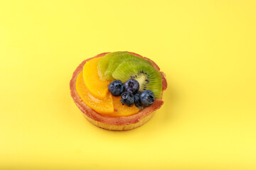 shortbread basket cake with cream, blueberries, peaches and kiwi on a plate on a yellow background