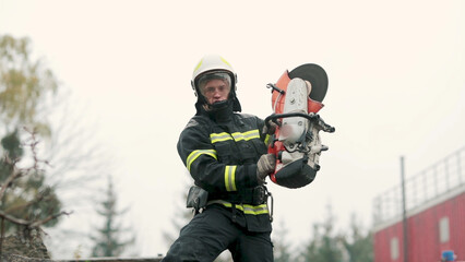 A firefighter works in extreme conditions, wearing protective clothing and a helmet, demonstrating professionalism and precision. A fireman cuts metal with a special tool, causing a powerful stream of