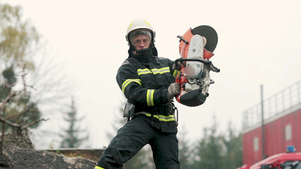 A firefighter works in extreme conditions, wearing protective clothing and a helmet, demonstrating professionalism and precision. A fireman cuts metal with a special tool, causing a powerful stream of