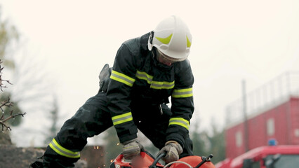 A firefighter works in extreme conditions, wearing protective clothing and a helmet, demonstrating professionalism and precision. A fireman cuts metal with a special tool, causing a powerful stream of