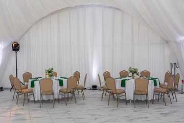 Wine glasses, silver tableware and green napkins on round tables covered with white tablecloth.