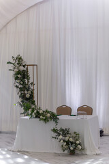 Wine glasses, silver tableware and green napkins on round tables covered with white tablecloth.