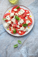 Plate of tomato and blue cheese salad, vertical shot on a blue and beige stone background, vertical shot with space