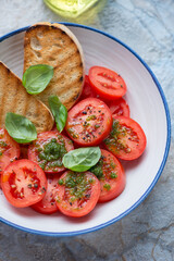 Tomato salad with basil oil, fresh green basil and grilled ciabatta in a blue and white plate, vertical shot, middle close-up