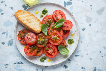 Plate with sliced red tomatoes, basil oil and ciabatta, horizontal shot on a white and blue granite background, elevated view