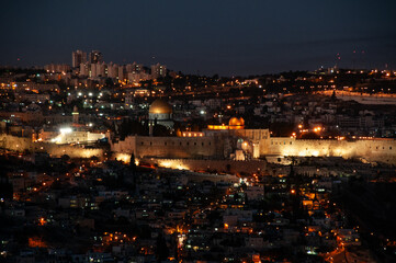 Panoramic view of the ancient walls of the Old City of Jerusalem with the golden Dome of the Rock shrine illuminated at twilight.