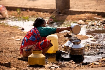 Woman collecting water from puddle, India © abc foto