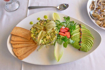 A gourmet avocado salad served on a white platter, accompanied by toasted bread, endive leaves, strawberries, and avocado slices, garnished with microgreens and colorful decoration
